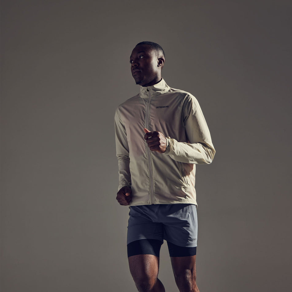 Front view of a model wearing the GOREWEAR Men's Concurve Windbreaker in the Tech Beige colourway. Model is also wearing shorts. (8604901965986)