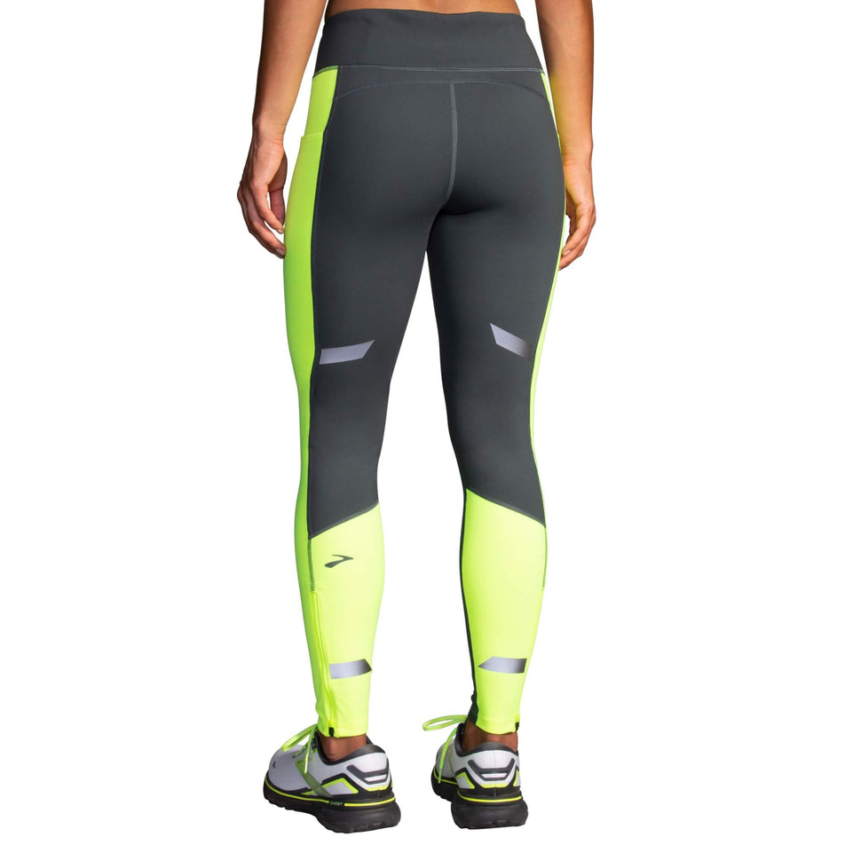 Back view of a model wearing a pair of Brooks Women's Run Visible Thermal Tights in the Asphalt/Nightlife colourway. Model is also wearing a pair of Brooks running shoes. (8065569194146)