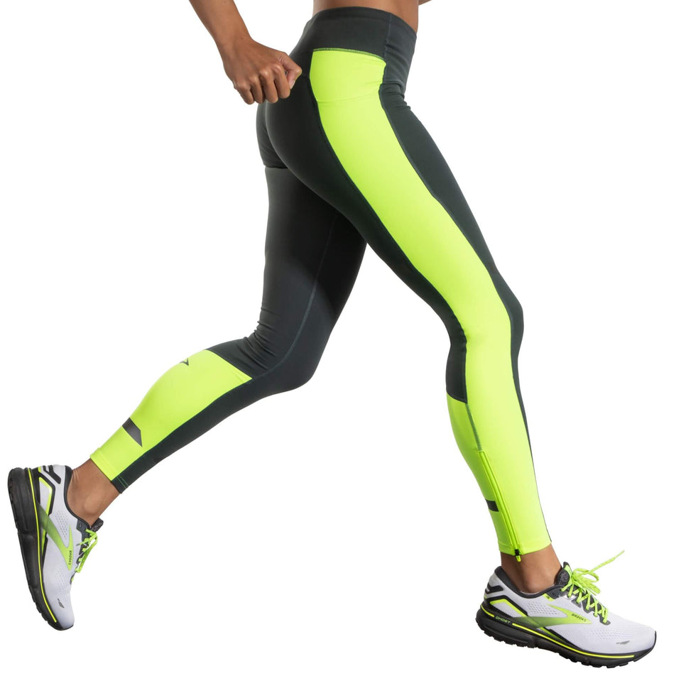 Side view of a model wearing a pair of Brooks Women's Run Visible Thermal Tights in the Asphalt/Nightlife colourway. Model is also wearing a pair of Brooks running shoes. (8065569194146)