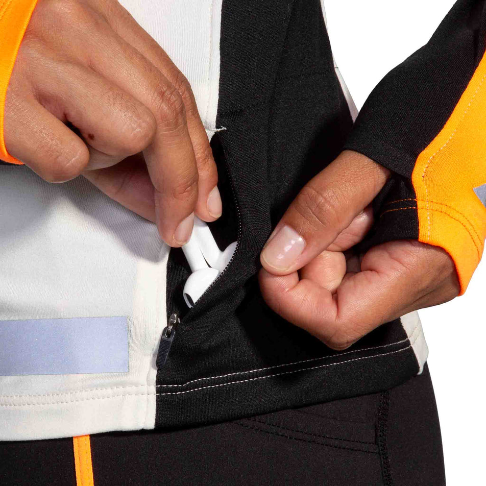 The zippered pocket on the left side of the Brooks Women's Run Visible 1/2 Zip 2.0 in the Ecru/Fluoro Flash/Black colourway. (8499447333026)