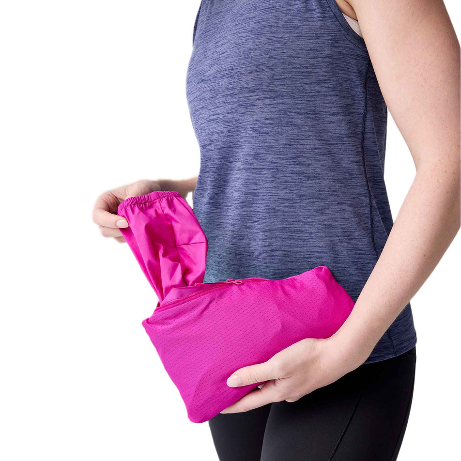 The model demonstrating the packability of the Brooks Women's Canopy Jacket 2.0 in the Magenta colourway. (8718875951266)