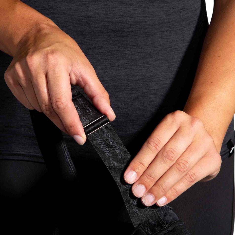 A model demonstrating the adjustable straps on the Brooks Women's Convertible 2.0 Sports Bra in the Black colourway. (8636795551906)