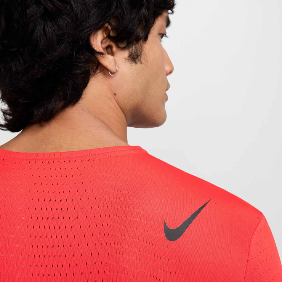 Close up view of the Nike SWOOSH on the back right shoulder section of the Nike Men's AeroSwift Dri-FIT ADV Short-Sleeve Running Top in the Light Crimson/Black colourway. (8560409706658)
