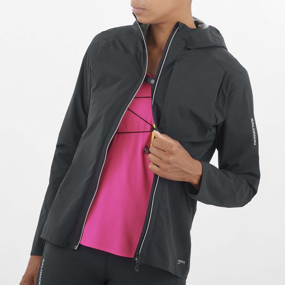 Close-up front view of a model wearing a Salomon Women's Bonatti Trail Jacket in the Deep Black colourway. Model has the jacket unzipped but the front sides are attached to each other via the fastener at the chest. (8157861019810)