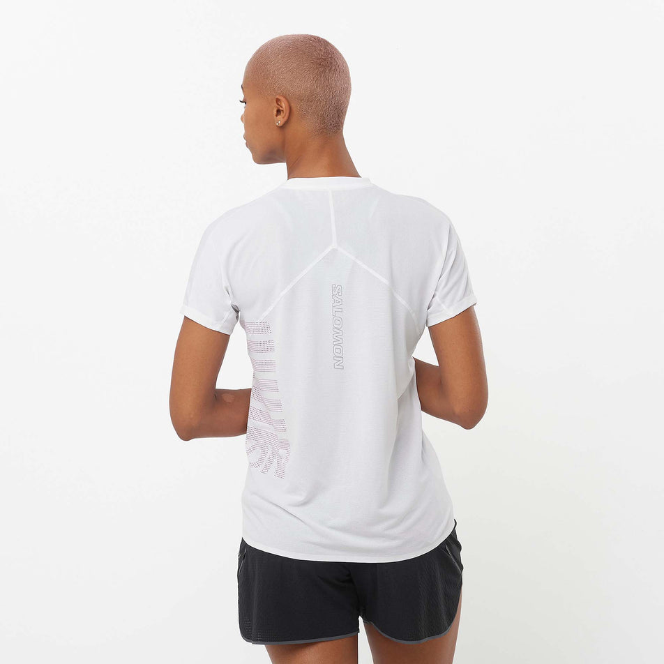 Back view of a model wearing a Salomon Women's Sense Aero GFX Short Sleeve Tee in the White/Beetroot Purple colourway. Model is also wearing Salomon running shorts. (8157870850210)