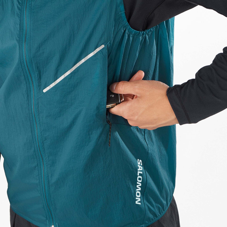 A model wearing demonstrating that there is a zipped pocket on the front left side of a Salomon Men's Sense Aero Wind Vest in the Deep Dive colourway (8157820977314)