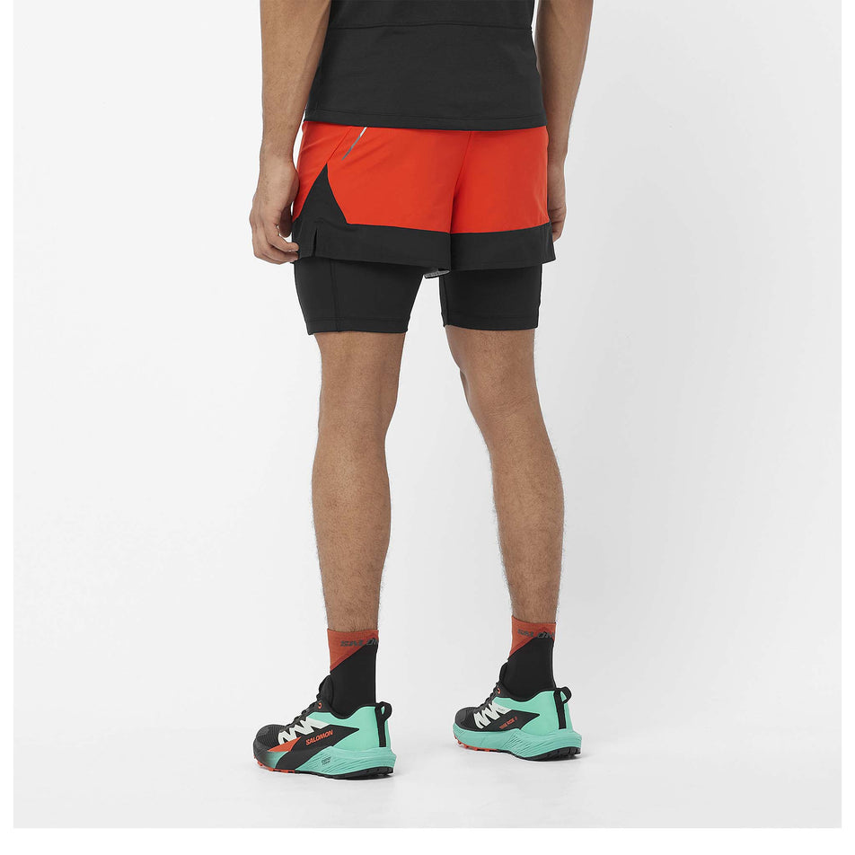 Back view of a model wearing a pair of Salomon Men's Cross 2in1 Shorts in the Cherry Tomato/Deep Black colourway. Model is also wearing shoes, socks and a t-shirt. (8467295436962)