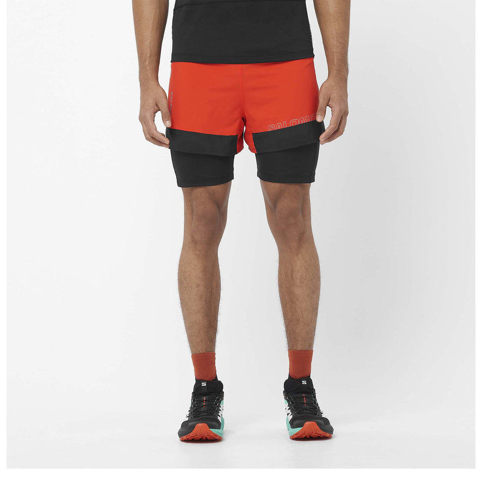 Front view of a model wearing a pair of Salomon Men's Cross 2in1 Shorts in the Cherry Tomato/Deep Black colourway. Model is also wearing shoes, socks and a t-shirt. (8467295436962)