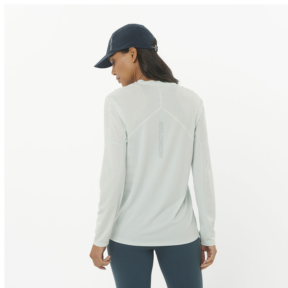 Back view of a model wearing a Salomon Women's Sense Aero Graphic Long Sleeve T-Shirt in the Misty Blue/White colourway. Model is also wearing a cap and leggings. (8464072999074)