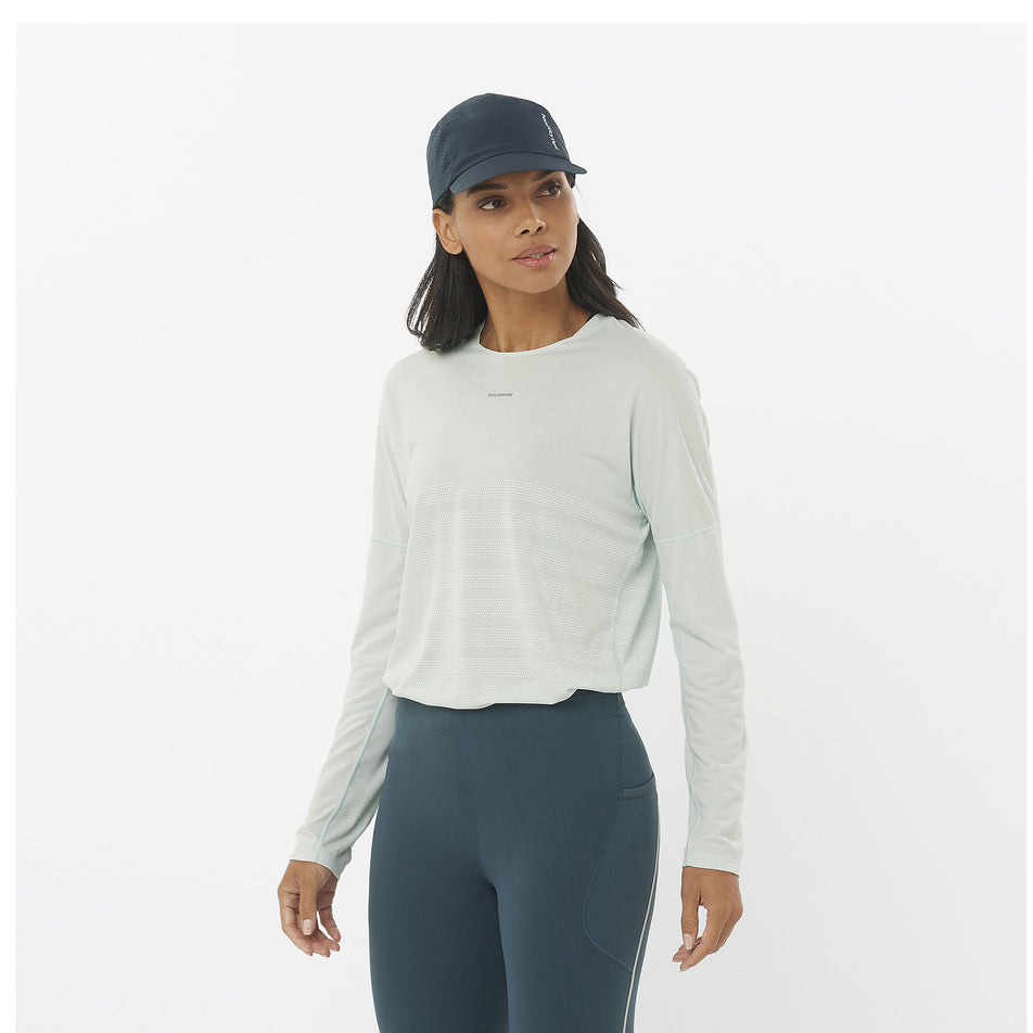 Front view of a model wearing a Salomon Women's Sense Aero Graphic Long Sleeve T-Shirt in the Misty Blue/White colourway. Model is also wearing a cap and leggings. (8464072999074)