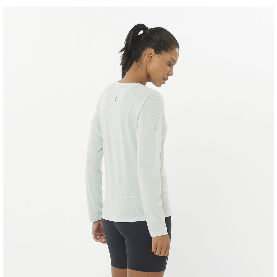 Back view of a model wearing a Salomon Women's Cross Run Long Sleeve T-Shirt in the Misty Blue colourway. Model is also wearing shorts. (8464163733666)