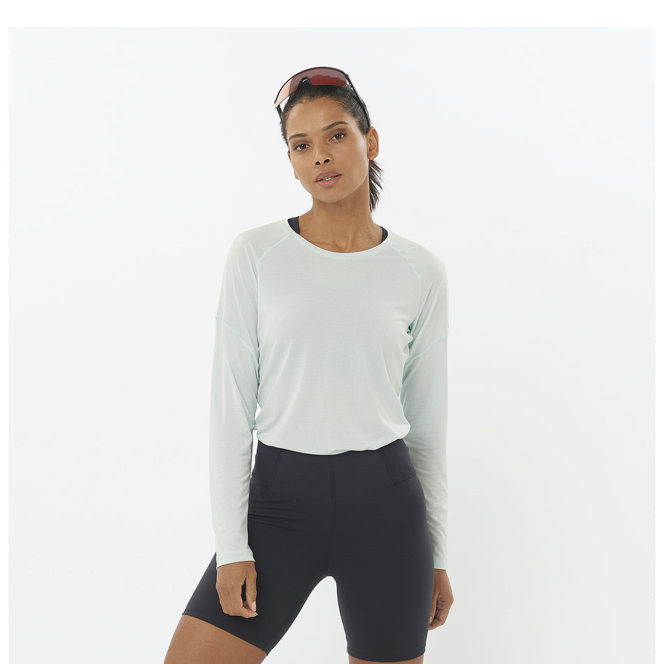 Front view of a model wearing a Salomon Women's Cross Run Long Sleeve T-Shirt in the Misty Blue colourway. Model is also wearing shorts and sunglasses. (8464163733666)