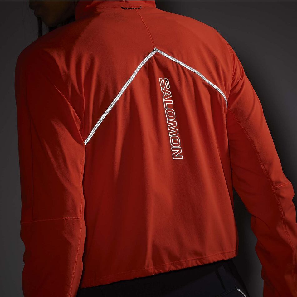 Back view of the reflective details on a back of a Salomon Women's Sense Aero Hybrid Cropped Half Zip Midlayer in the Cherry Tomato colourway. Top is being worn by a model. (8462927102114)