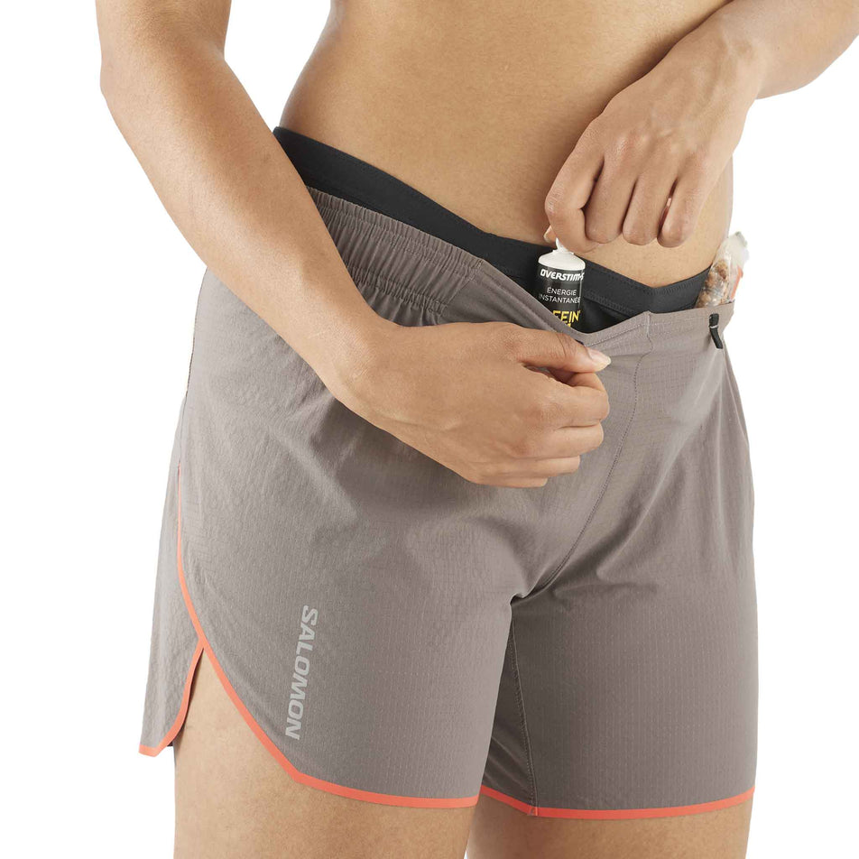 Front view of a model demonstrating that nutrition can be stored in the front stretch pocket on the waistband of a pair of Salomon Women's Sense Aero 5