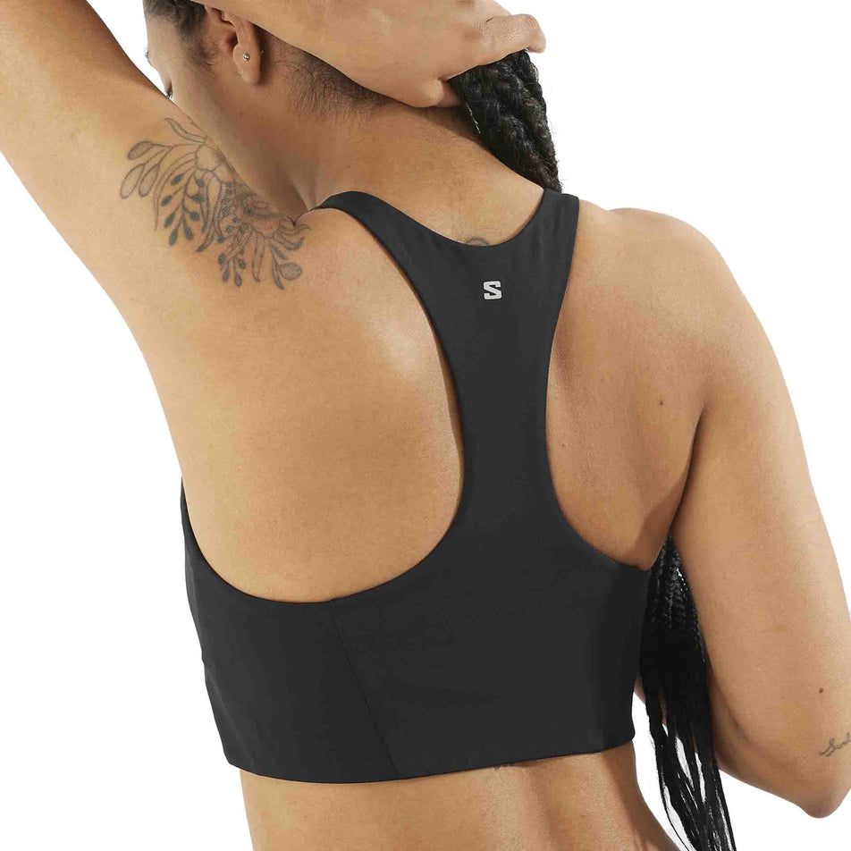 Back view of a model wearing the Salomon Women's SHKout CORE Sports Bra in the Deep Black colourway. (8574537859234)