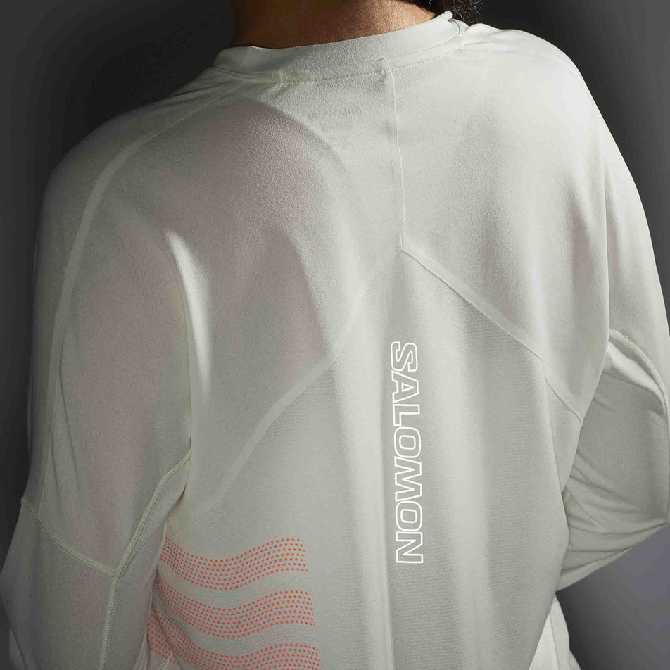 The reflective Salomon logo on the back of the Salomon Women's Sense Aero Graphic Long Sleeve T-Shirt in the Icicle/Neon Flame colourway. (8574193696930)