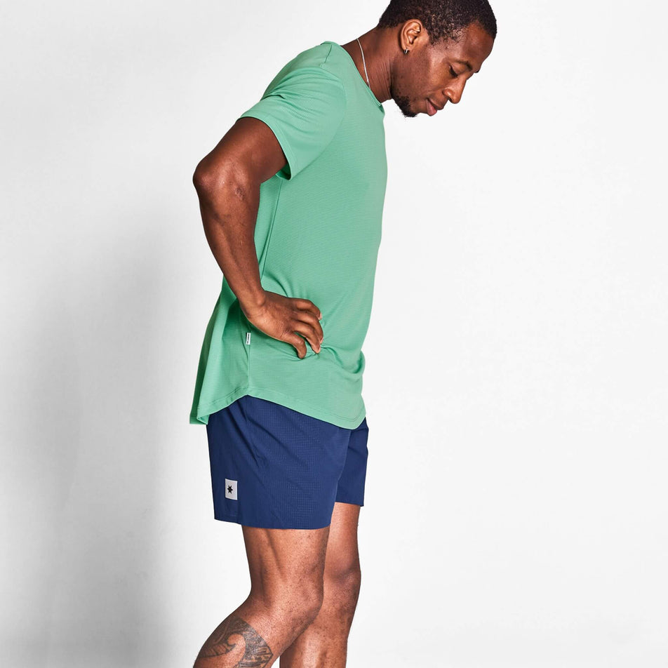 Side view of a model wearing a SAYSKY Men's Reactive Flow T-Shirt in the Green AOP colourway. Model is also wearing shorts. (8628407533730)