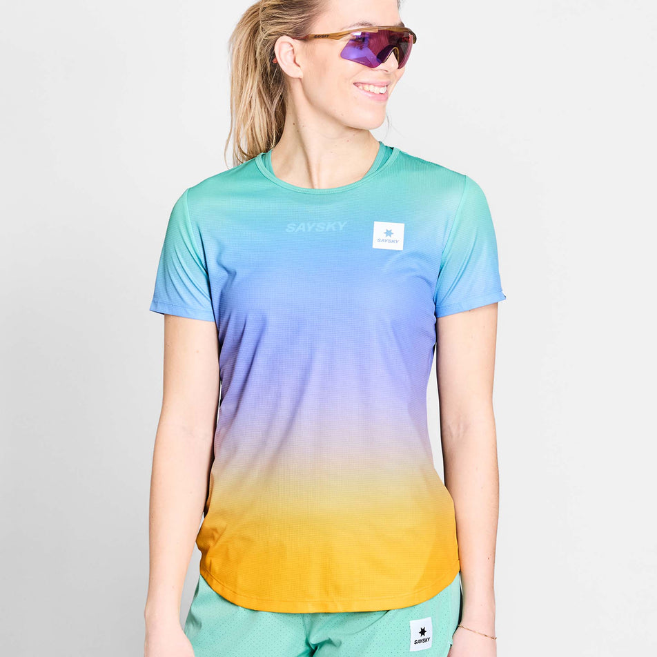 Front view of a model wearing the SAYSKY Women's Drip Dye Flow T-Shirt in the Purple AOP colourway. Model is also wearing sunglasses and shorts. (8675475030178)