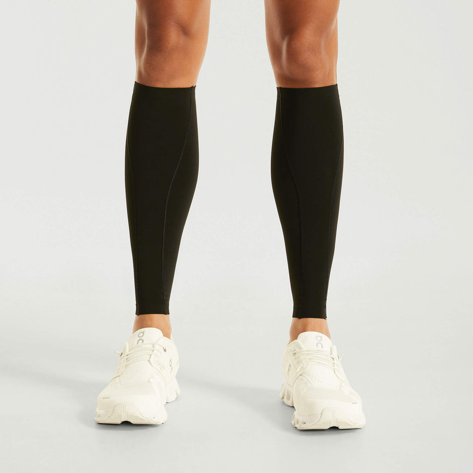 Front view of a model wearing the Pressio Unisex EQ Compression Calf Guards in the Black colourway. Model is also wearing shoes. (8475847393442)