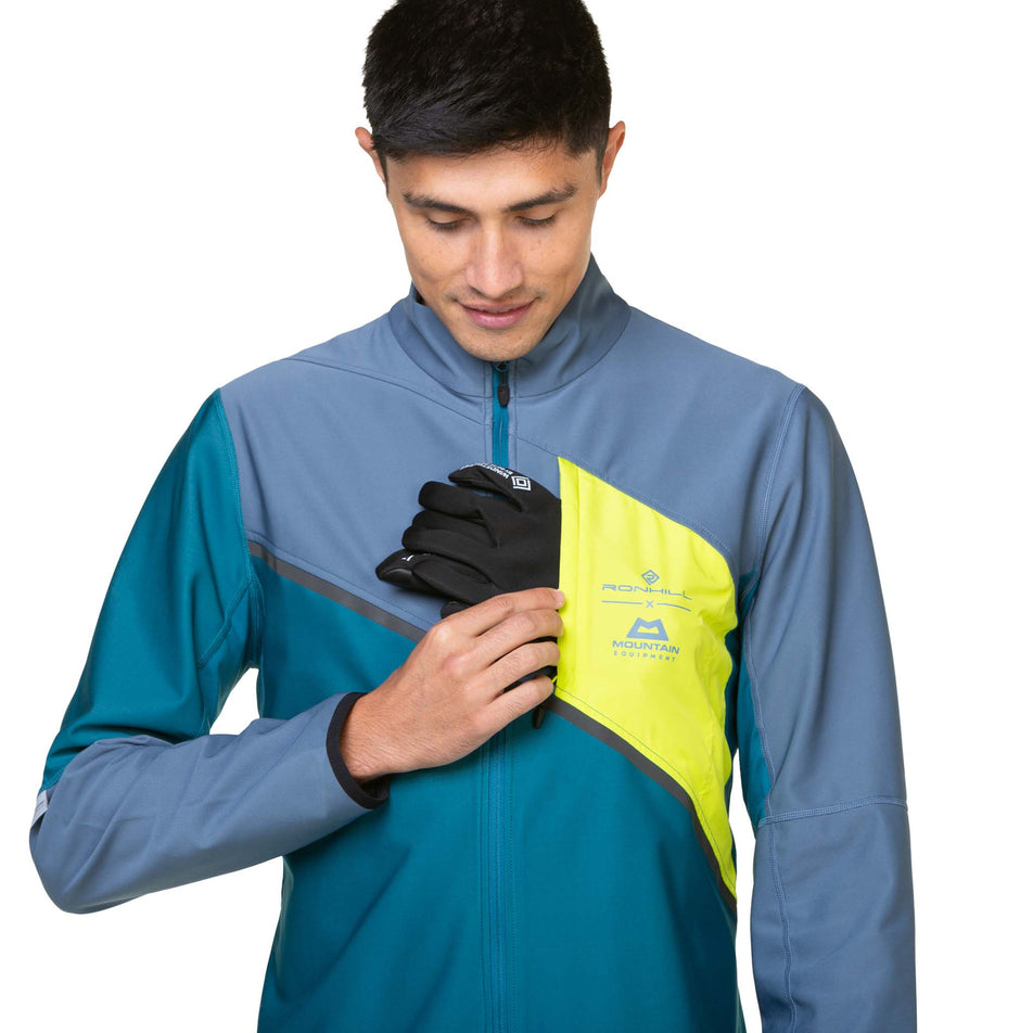 A model demonstrating that gloves can be stored in the chest pocket of a Ronhill Men's Tech GORE-TEX Windstopper Jacket in the Deep Teal/Lake Acid colourway. Jacket is being worn by a model. (8470614016162)